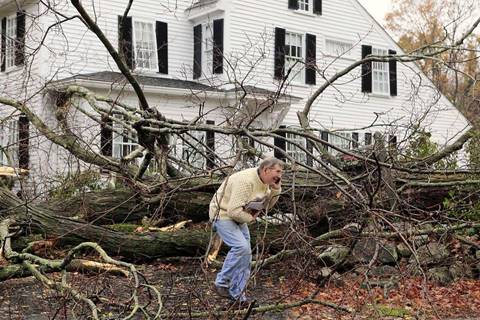 John Constantine makes his way out of his house after winds from Hurricane Sandy toppled a tree fell onto it in Andover, Mass., in 2012. Photo: Winslow Townson, Associated Press